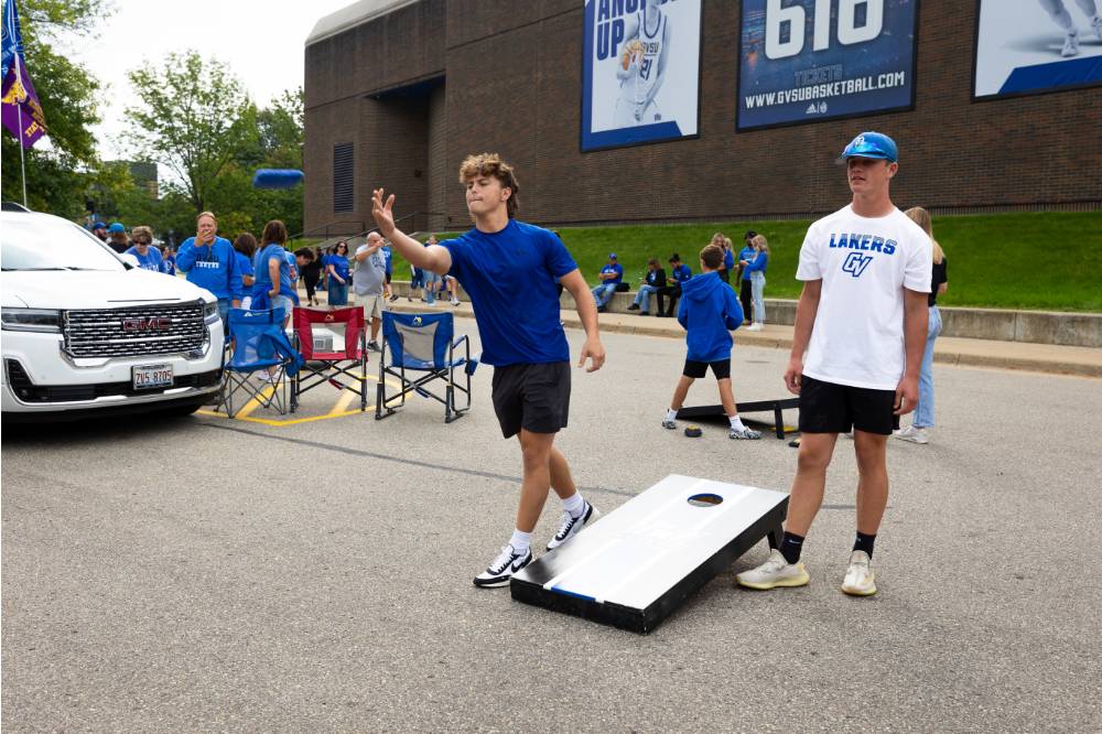 Students play cornhole game in tailgate parking lot.
